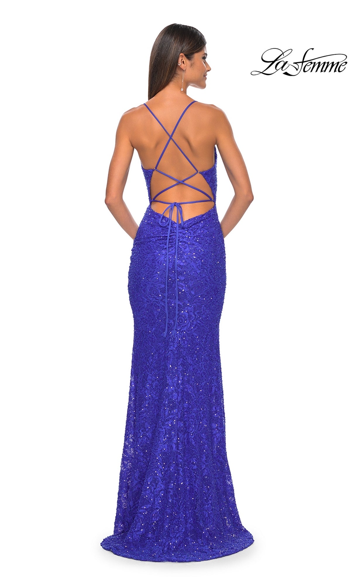 A woman wears the La Femme Long Beaded Lace Prom Dress 31359, a fitted, floor-length gown with a criss-cross lace-up open back in royal blue, standing against a white background.